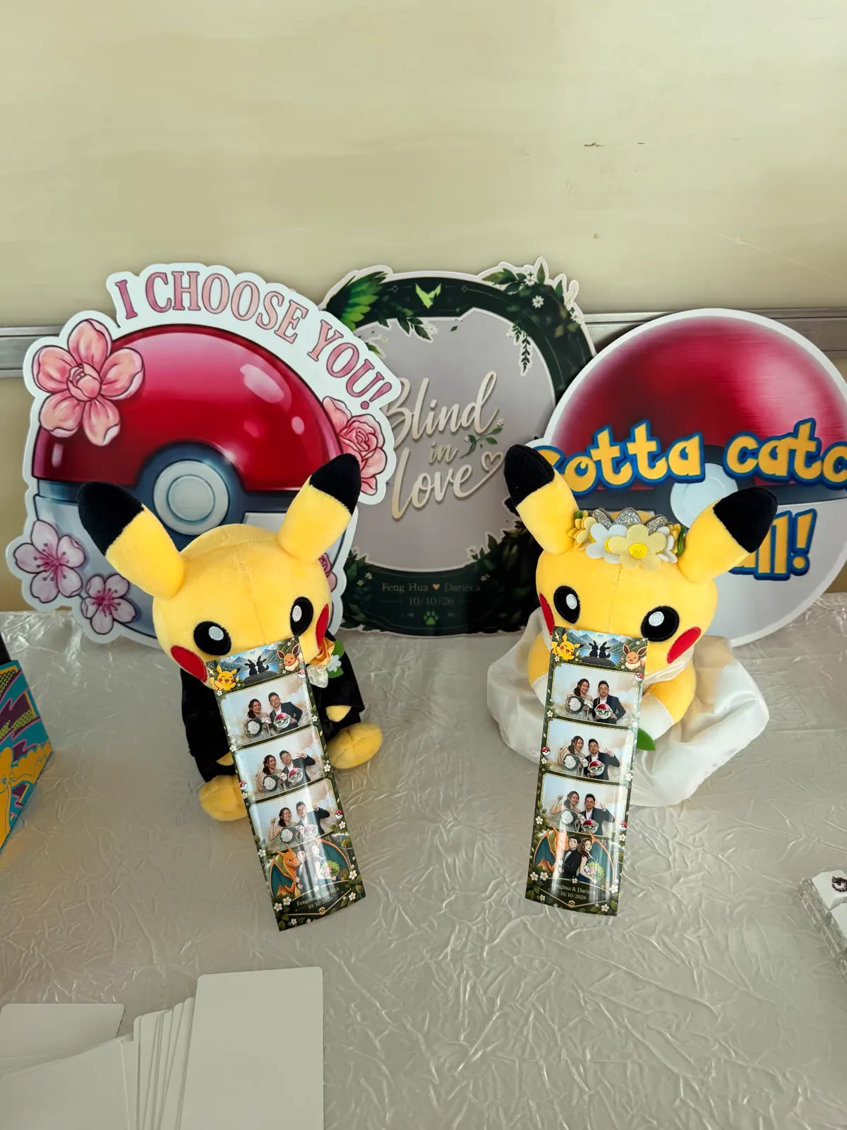 Custom wedding props with 'I Choose You!' and 'Blind in Love' signs beside plush toys holding printed photo strips