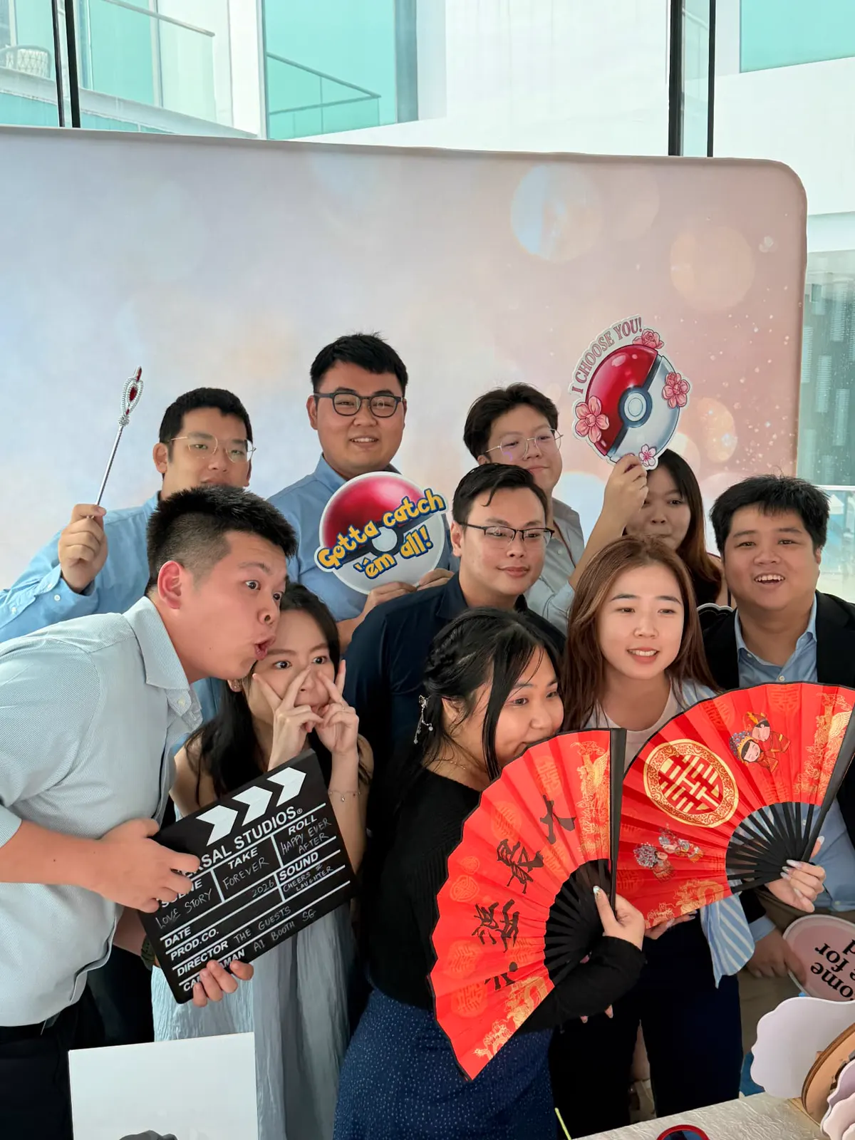 Wedding guests posing with a clapperboard, red wedding fans and custom signs at the photobooth backdrop