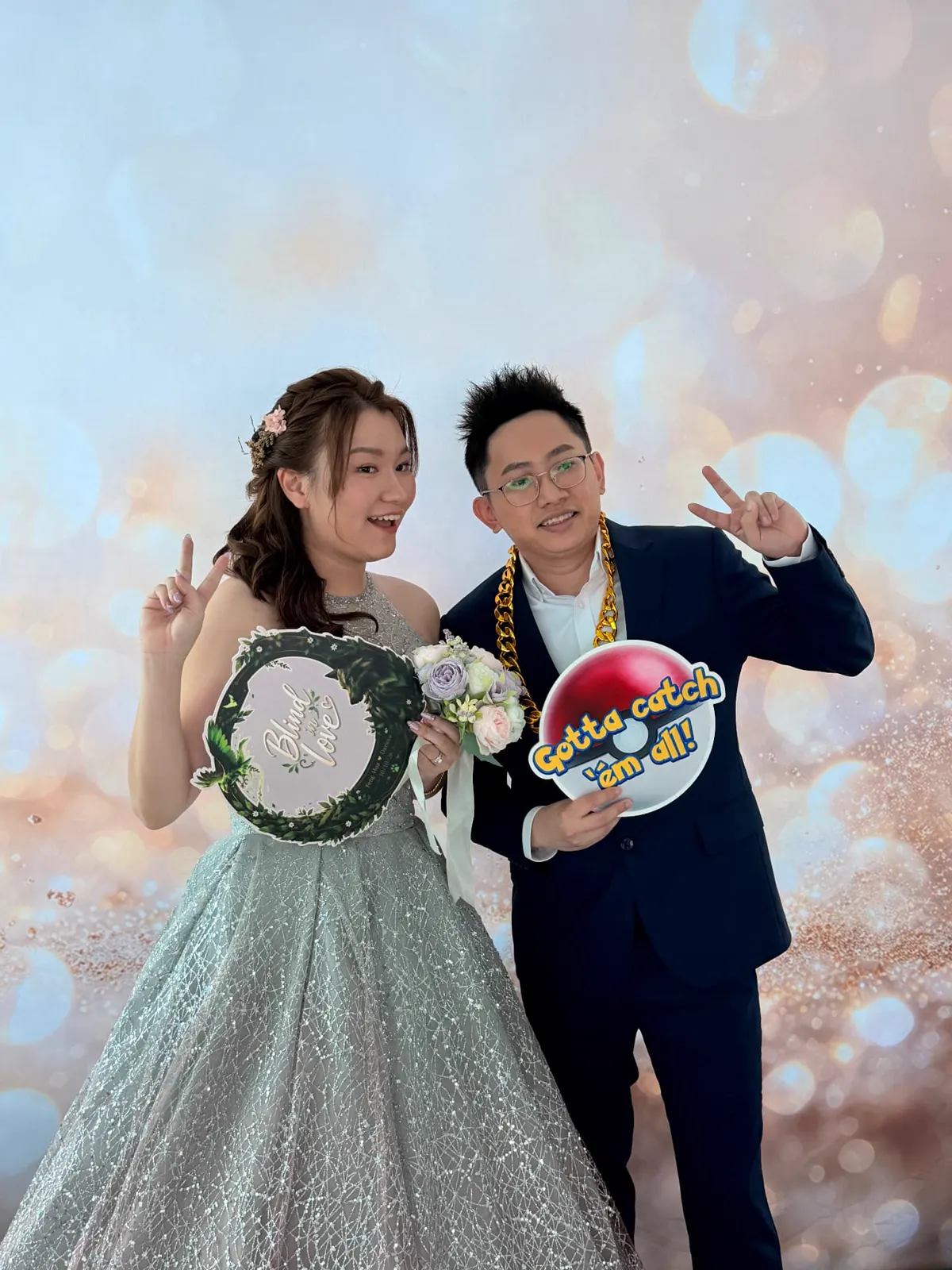 Bride and groom posing at the photobooth with a 'Blind in Love' sign and a 'Gotta catch 'em all!' prop